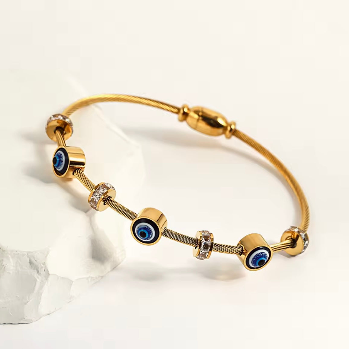 Gold bracelet with blue evil eye charms on a white background