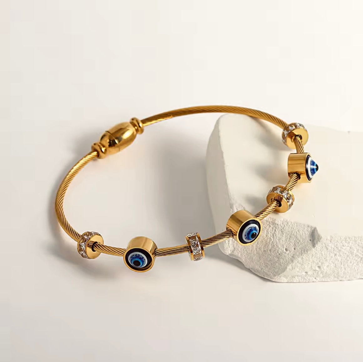 Gold bracelet with blue evil eye charms on a light background