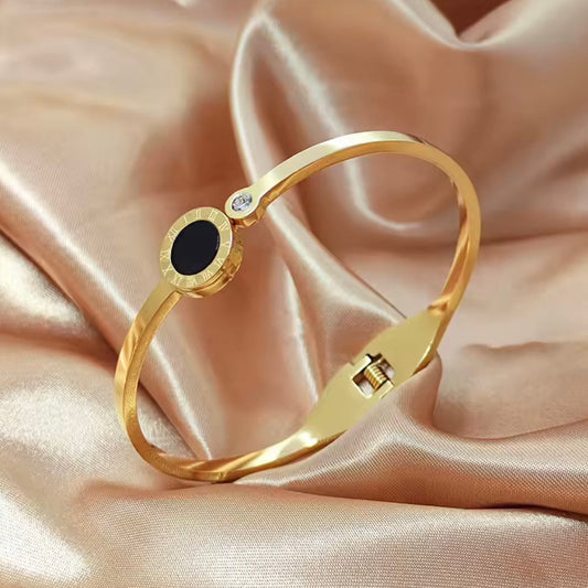 Gold bracelet with a black stone and clear gem on a pink satin background