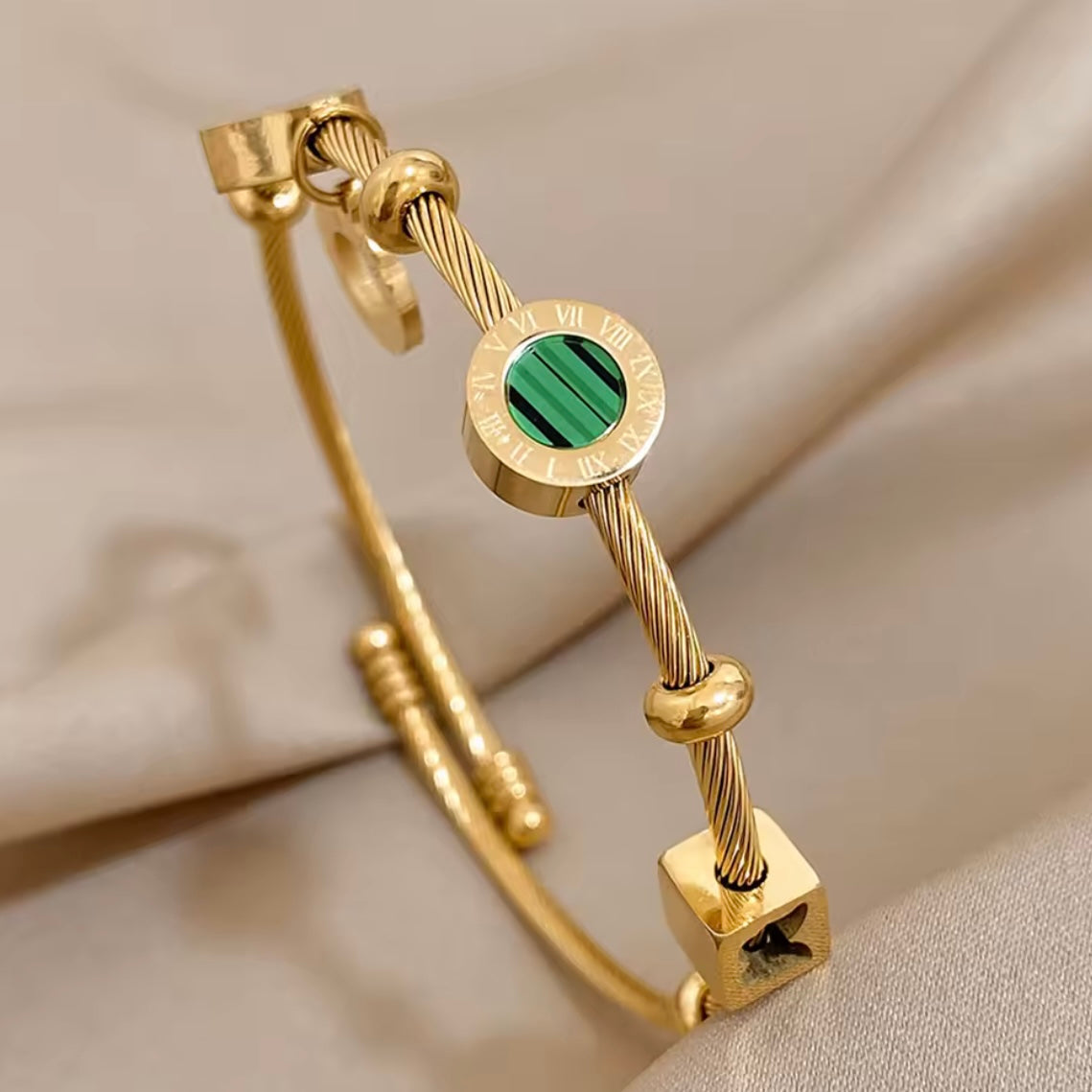 Gold bracelet with a green stone on a beige fabric background