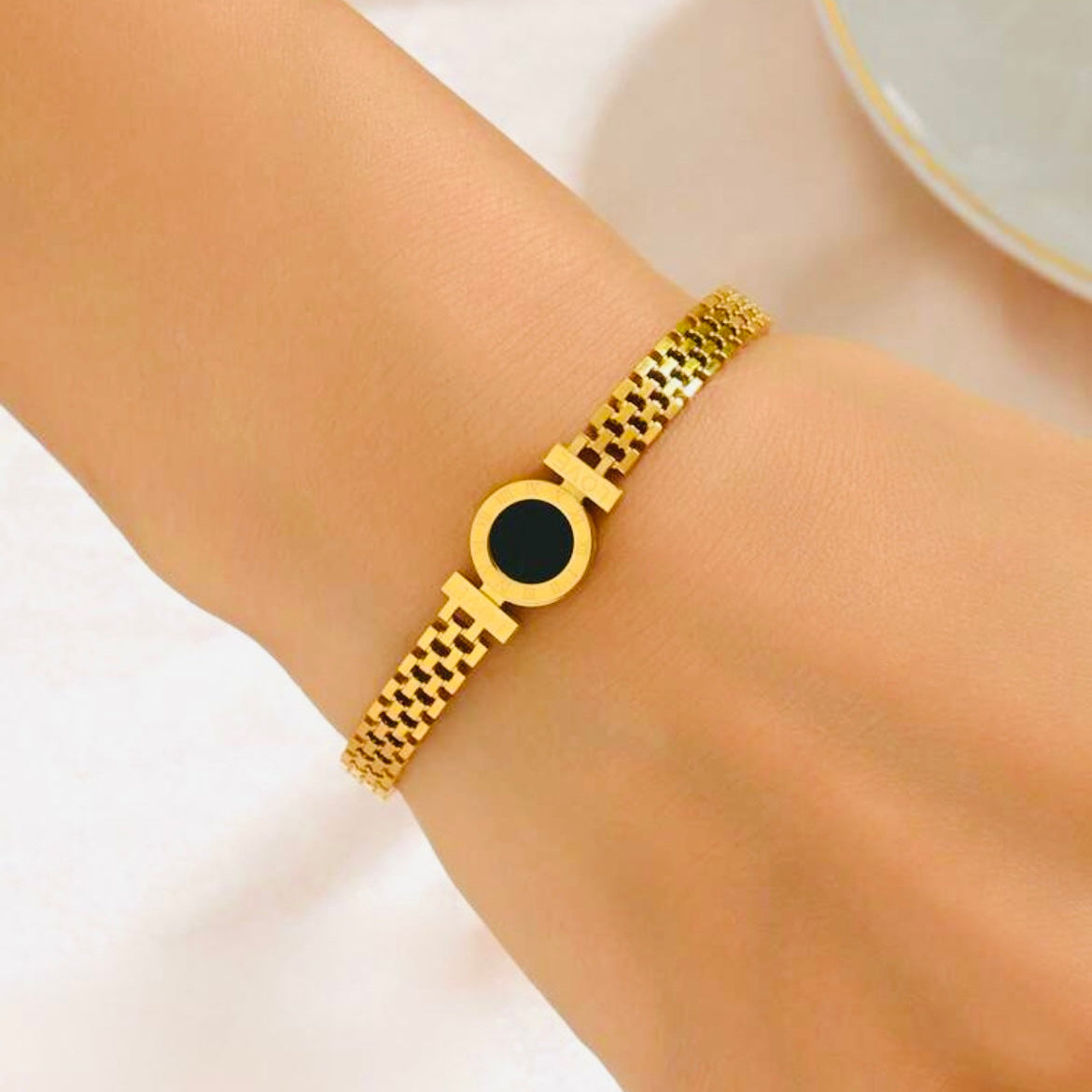 Gold bracelet with a black center on a wrist against a white background