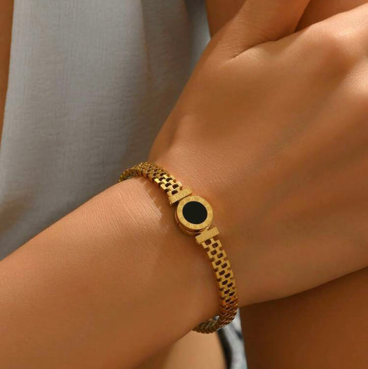 Gold bracelet with a black stone on a wrist against a neutral background