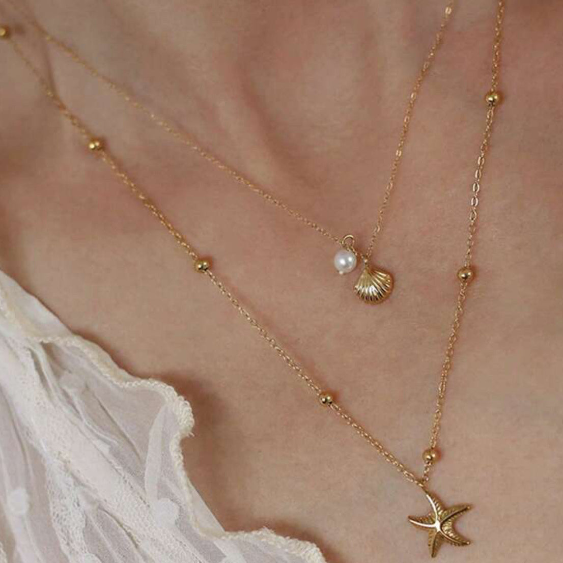 Gold necklace with starfish and shell pendant on a person wearing a white garment.