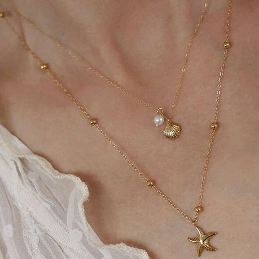 Gold necklace with starfish and shell pendant on a person wearing a white garment.