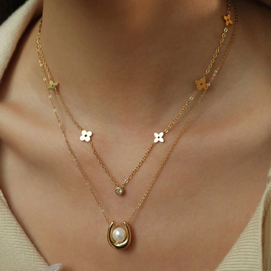 Gold necklace with floral and teardrop pendants on a person wearing a beige top.