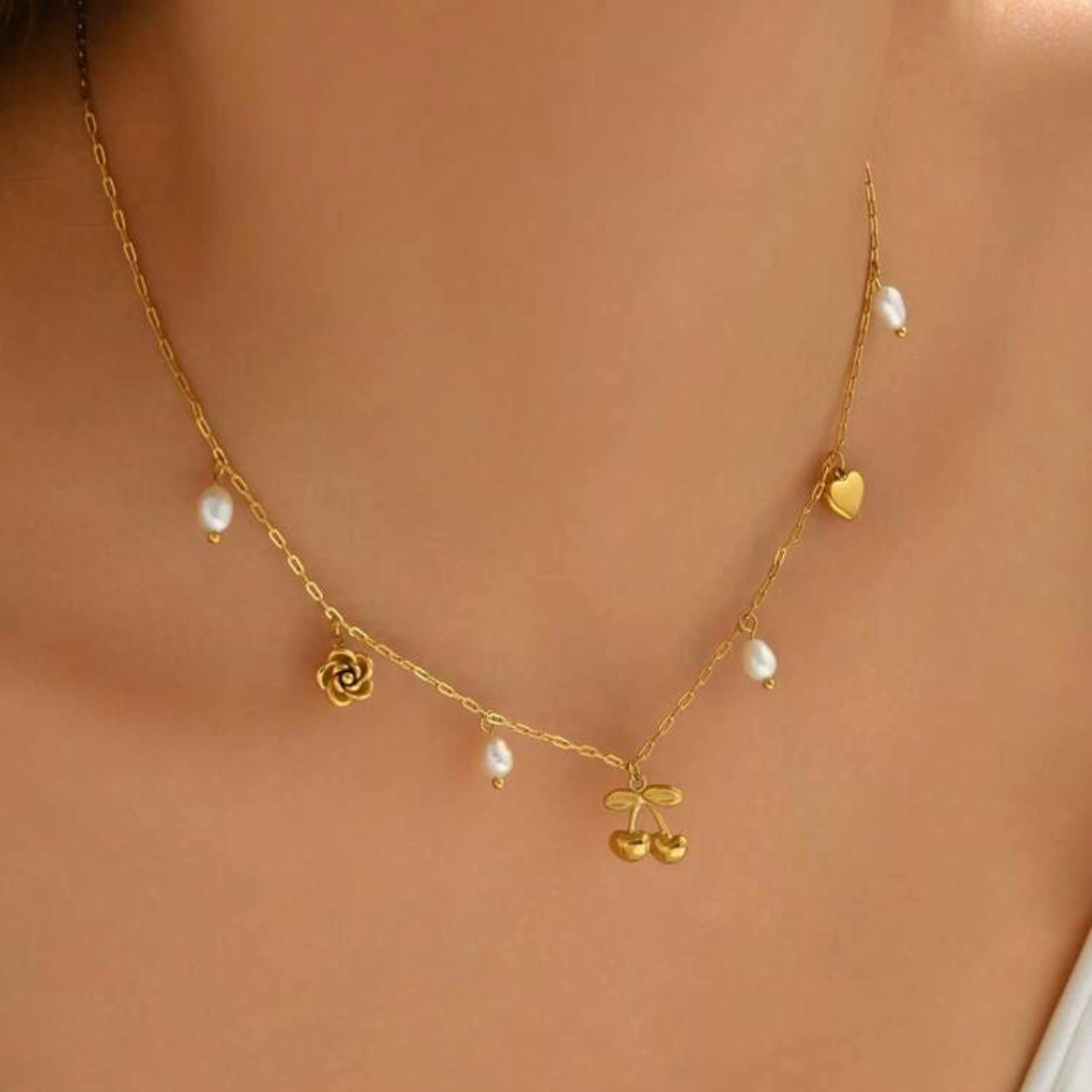 Gold necklace with floral and berry pendants on a skin-toned background