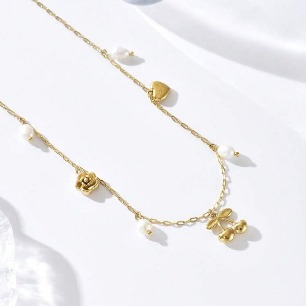 Gold necklace with floral and heart-shaped pendants on a white background