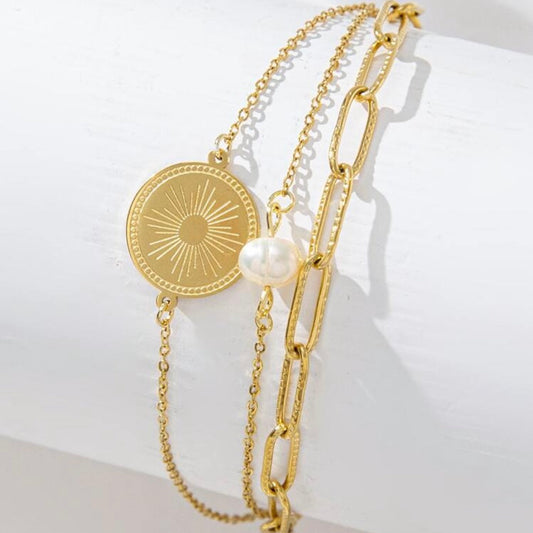 Gold bracelet with a coin charm and pearl bead on a white background