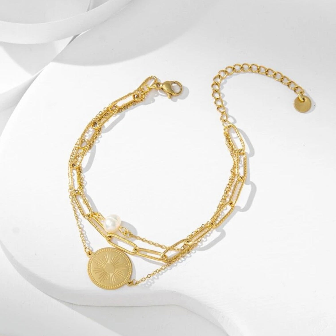 Gold bracelet with chain and circular charm on a white background