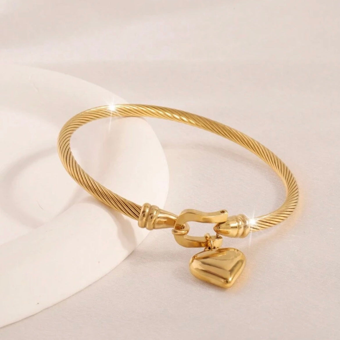 Gold bracelet with a heart-shaped clasp on a light background