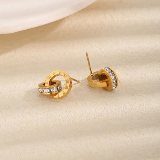 Gold earrings with embedded stones on a beige fabric background