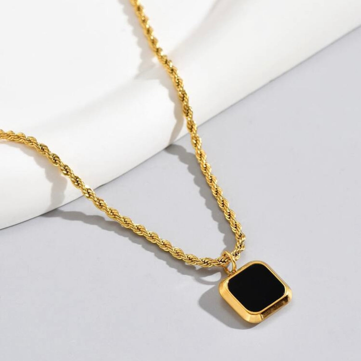 Gold necklace with a black square pendant on a light gray background