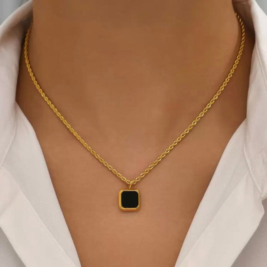 Gold necklace with a black square pendant on a neutral background
