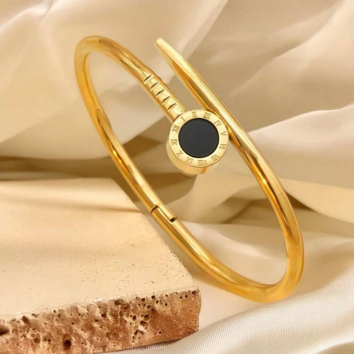 Gold bracelet with a black stone on a beige fabric background