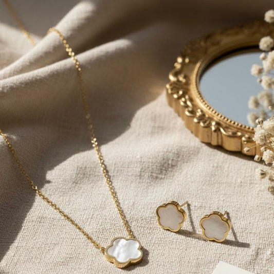 Gold necklace and earrings on a textured surface with a decorative mirror in the background.