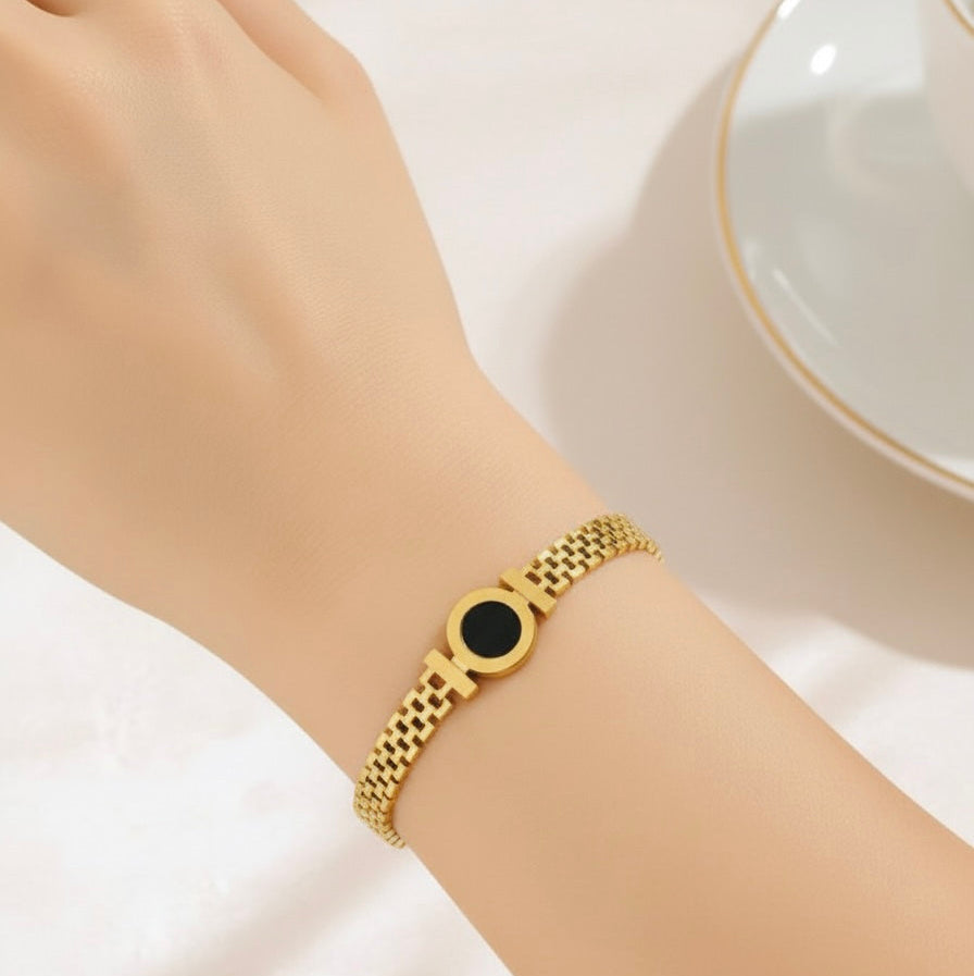 Gold bracelet with a black stone on a wrist against a white background