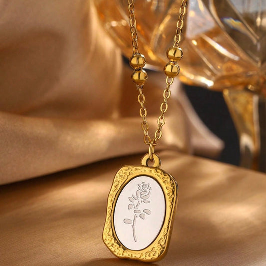 Gold necklace with a pendant featuring an engraved design on a soft, blurred background.