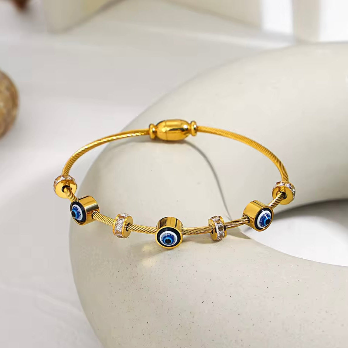 Gold bracelet with blue eye beads on a white stone surface