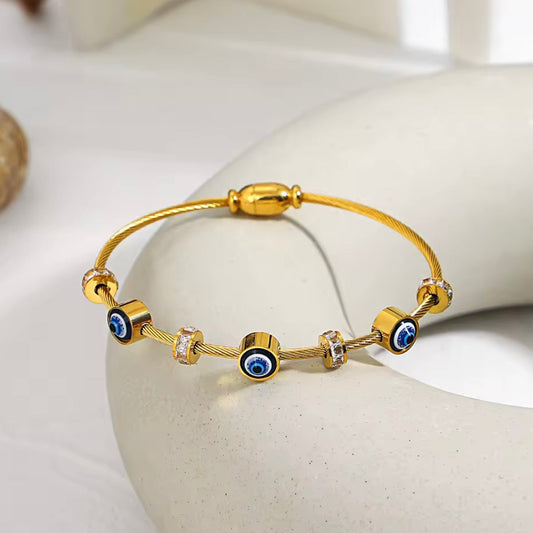 Gold bracelet with blue eye beads on a white stone surface