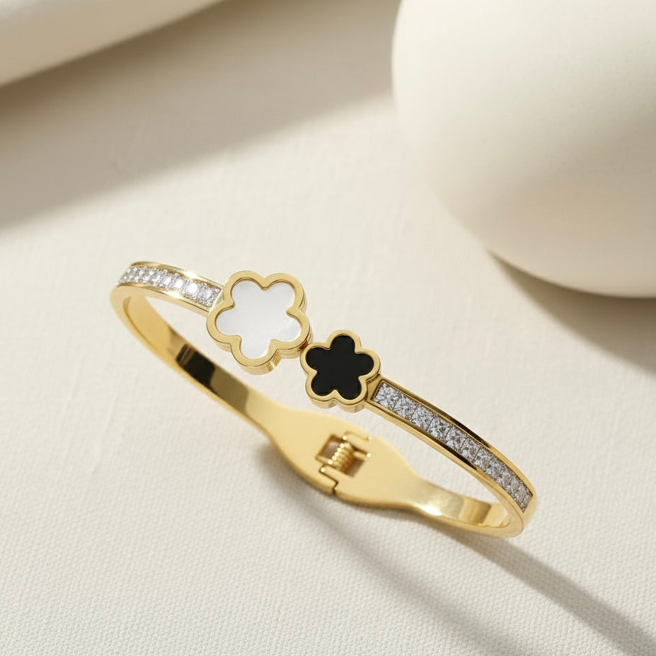 Gold bracelet with clover and black stone design on a beige surface