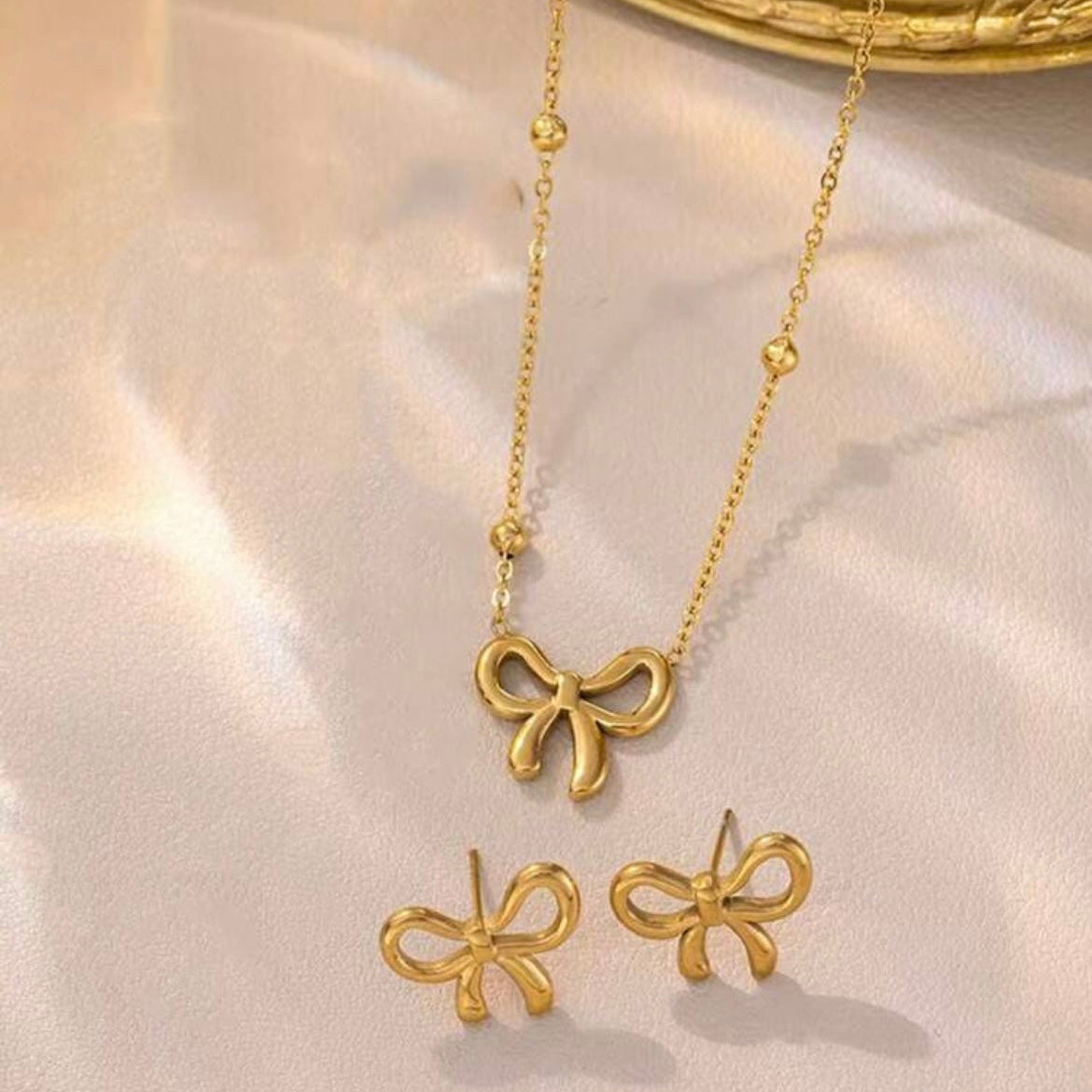 Gold bow-shaped necklace and earrings on a light pink background