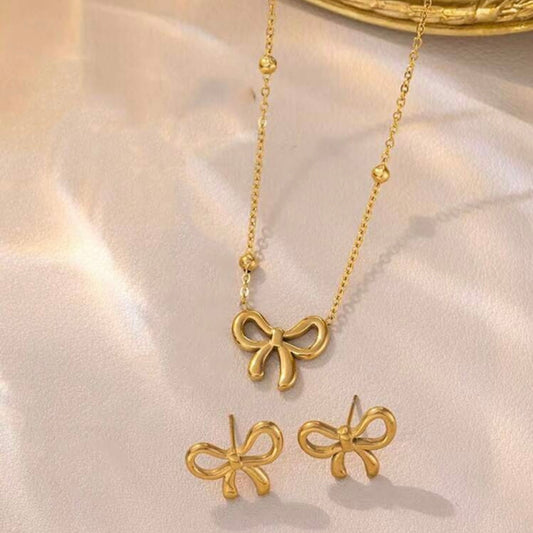 Gold bow-shaped necklace and earrings on a light pink background