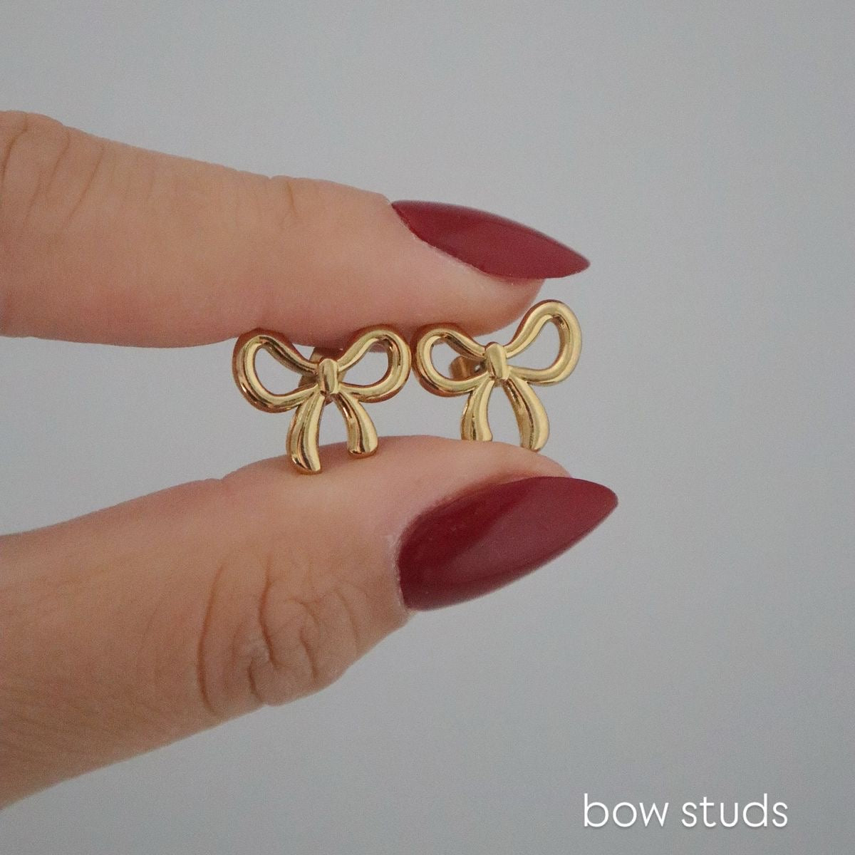 Gold bow-shaped earrings held between fingers against a plain background