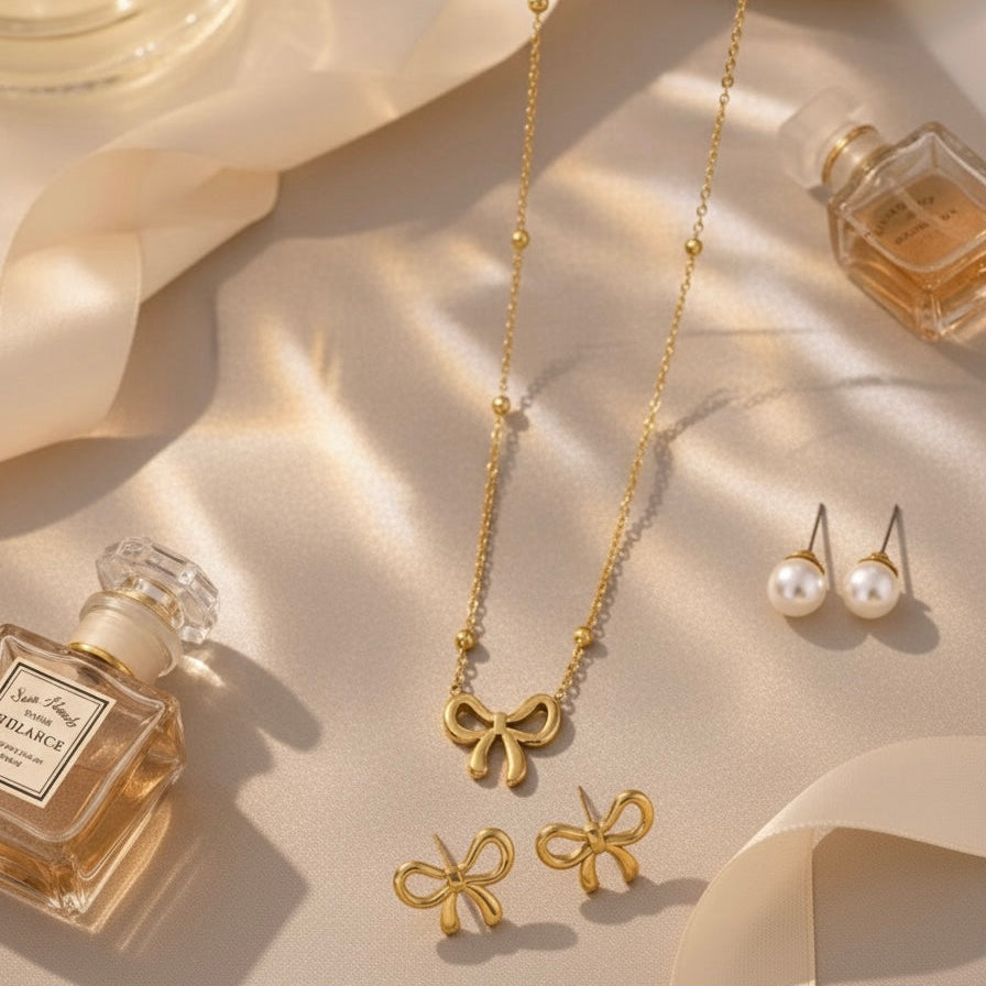 Gold bow necklace and earrings with perfume bottles on a soft beige fabric background